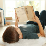 Cute schoolboy with book on carpet on floor